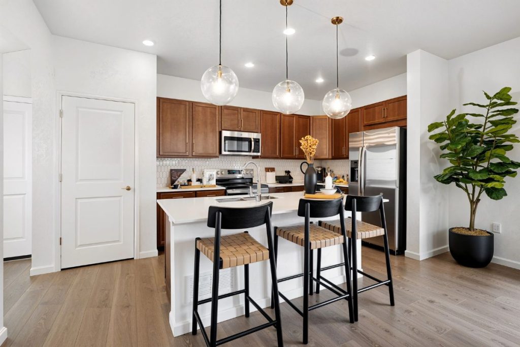 Modern kitchen interior with white countertops, dark wood cabinets, pendant lighting, and stainless steel appliances in a contemporary open-concept home design