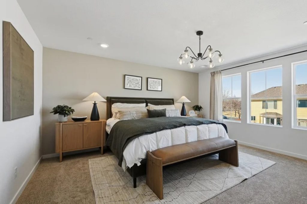 Spacious primary bedroom with large windows, neutral decor, modern lighting, and cozy seating creating a bright and relaxing home retreat
